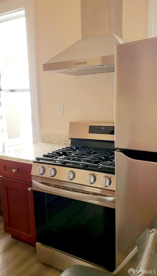 kitchen featuring a wealth of natural light, light hardwood / wood-style floors, wall chimney range hood, and appliances with stainless steel finishes