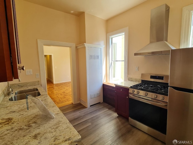 kitchen with sink, wall chimney exhaust hood, stainless steel fridge, range with gas stovetop, and light stone counters