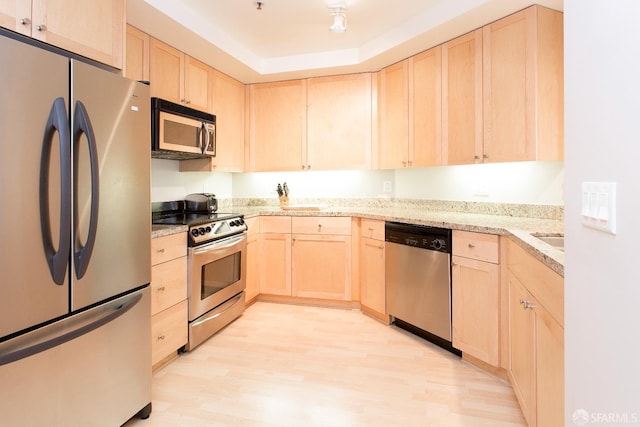 kitchen with stainless steel appliances, a raised ceiling, light wood-type flooring, and light brown cabinetry