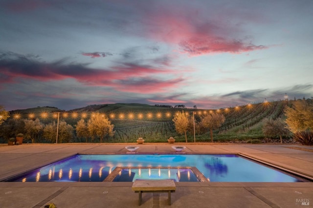 pool at dusk with a patio area, a mountain view, and a pool with connected hot tub