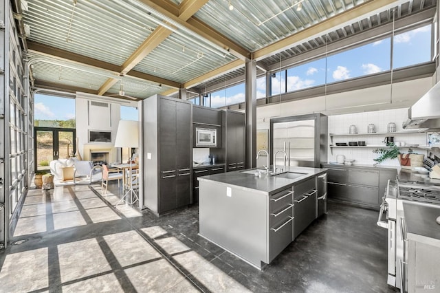 kitchen featuring modern cabinets, a sink, appliances with stainless steel finishes, a kitchen island with sink, and a fireplace