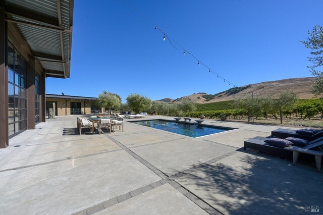 outdoor pool with a mountain view, outdoor dining space, and a patio area