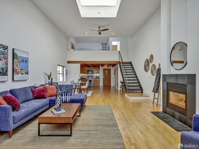 living room featuring ceiling fan, a skylight, hardwood / wood-style flooring, a high ceiling, and a fireplace