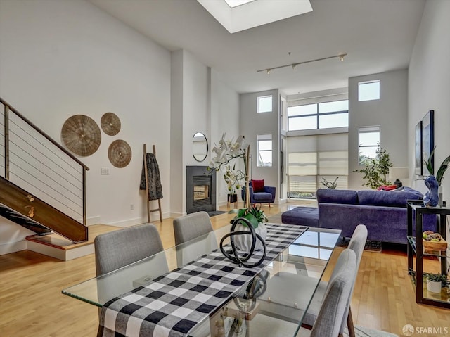 dining room with a skylight, light wood-type flooring, a towering ceiling, and track lighting