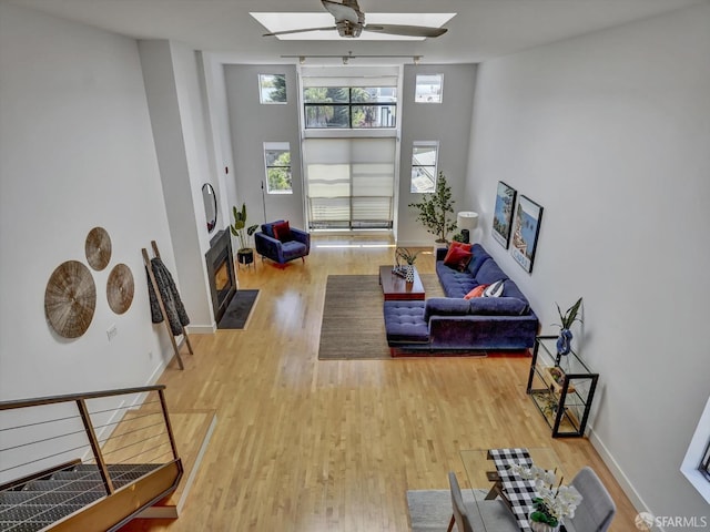 living room featuring a high ceiling, ceiling fan, light hardwood / wood-style flooring, and a skylight