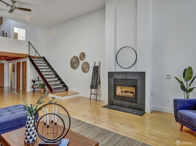 living room with ceiling fan, a tiled fireplace, and wood-type flooring