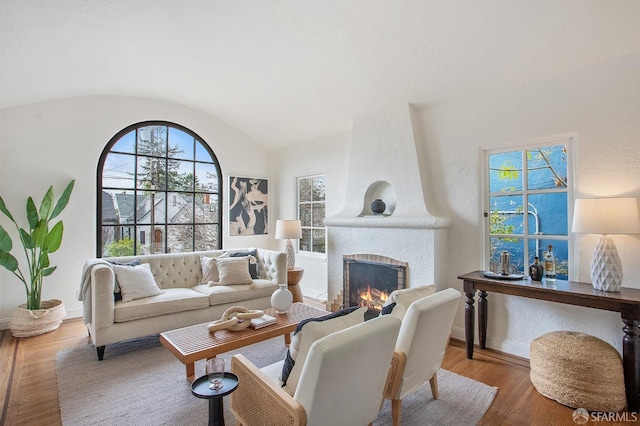 living room with hardwood / wood-style flooring, lofted ceiling, and a large fireplace