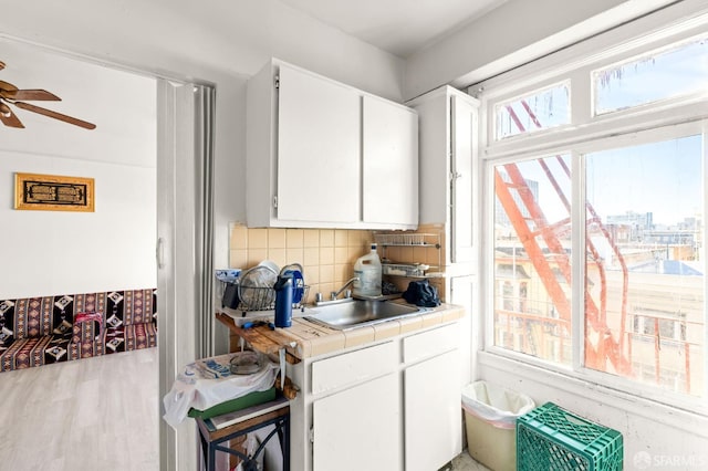 kitchen with decorative backsplash, ceiling fan, sink, white cabinets, and tile counters