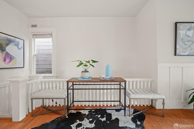 sitting room with wainscoting, visible vents, a decorative wall, and wood finished floors