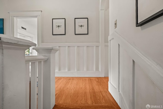 hall featuring wainscoting, wood finished floors, and a decorative wall