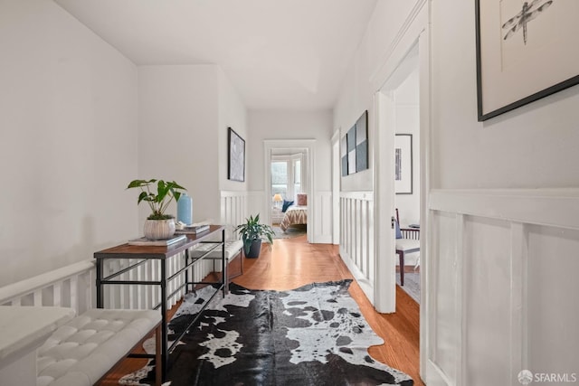 corridor with a wainscoted wall, a decorative wall, and wood finished floors