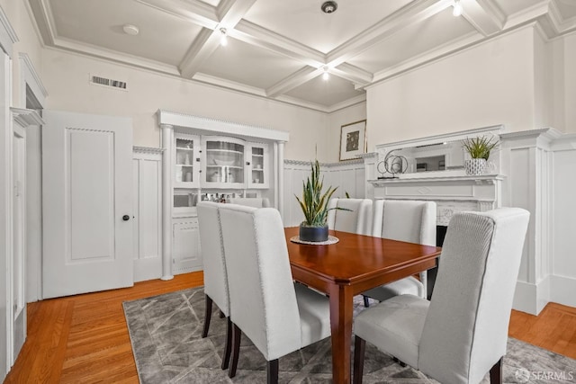 dining area featuring visible vents, coffered ceiling, wainscoting, beamed ceiling, and light wood-style floors