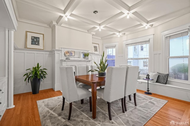 dining space with light wood finished floors, coffered ceiling, beam ceiling, and a decorative wall