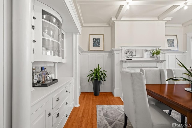 dining space with a wainscoted wall, ornamental molding, a decorative wall, and light wood-style floors