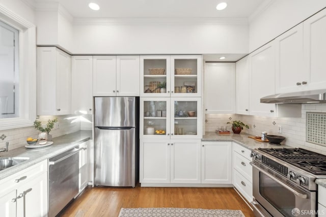 kitchen with white cabinets, glass insert cabinets, light stone counters, stainless steel appliances, and under cabinet range hood