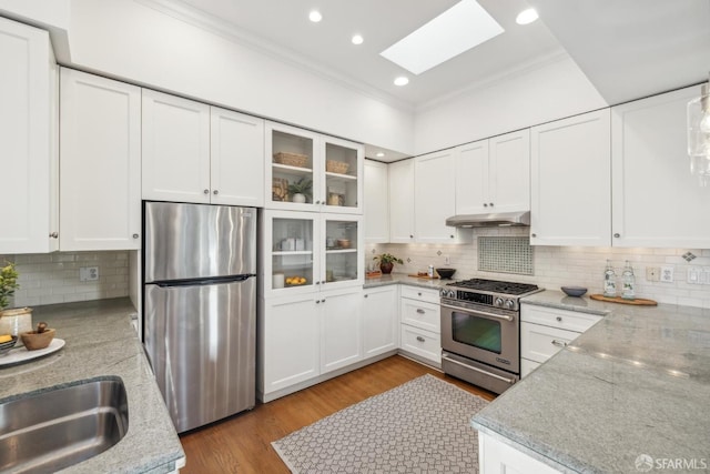 kitchen with light stone countertops, white cabinetry, glass insert cabinets, and stainless steel appliances