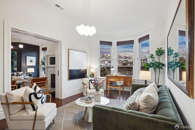 living area featuring dark wood finished floors, a fireplace, a notable chandelier, visible vents, and baseboards