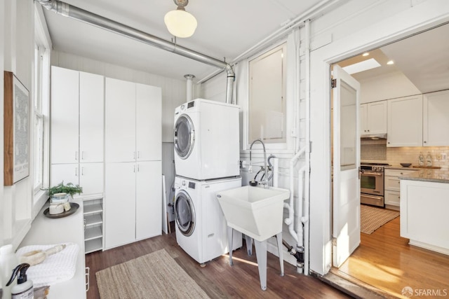 clothes washing area with stacked washer and dryer, cabinet space, and dark wood finished floors