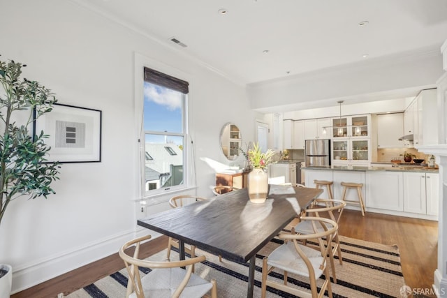 dining space featuring visible vents, crown molding, light wood-style flooring, and baseboards