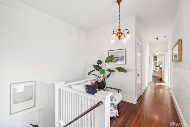 hallway with a wainscoted wall, dark wood finished floors, and a notable chandelier