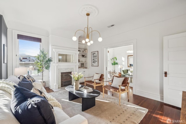 living room with built in shelves, visible vents, an inviting chandelier, a fireplace with flush hearth, and wood finished floors