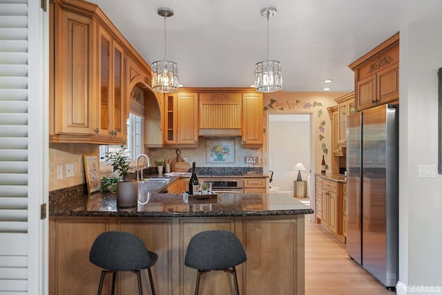 kitchen with appliances with stainless steel finishes, tasteful backsplash, light wood-type flooring, decorative light fixtures, and kitchen peninsula