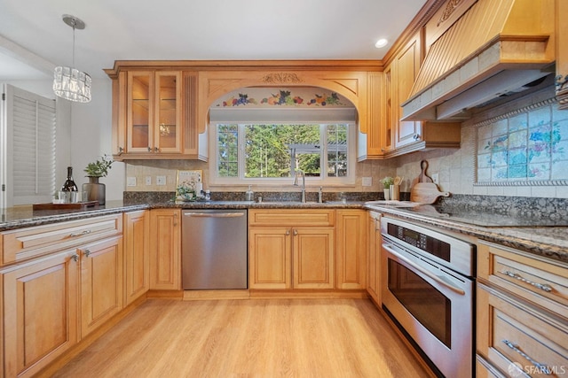 kitchen with hanging light fixtures, appliances with stainless steel finishes, custom exhaust hood, sink, and light wood-type flooring