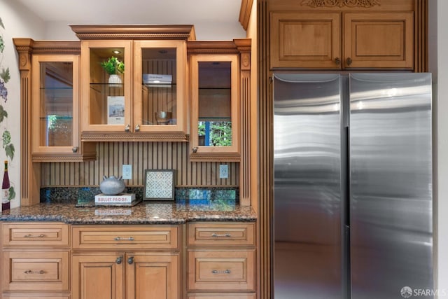 kitchen featuring dark stone countertops, backsplash, and stainless steel fridge