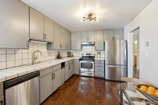 kitchen with tasteful backsplash, dark wood-style floors, stainless steel appliances, under cabinet range hood, and a sink