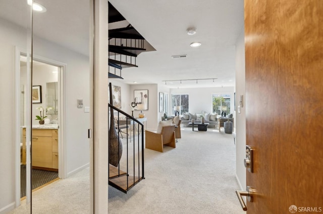 entryway featuring rail lighting, baseboards, stairway, and light colored carpet