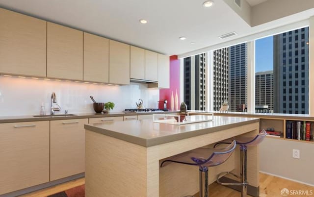 kitchen featuring sink, a kitchen bar, a center island, stainless steel gas cooktop, and cream cabinets