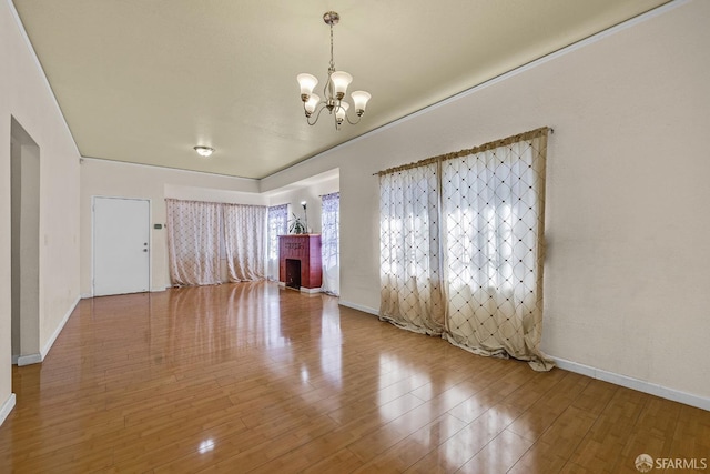 empty room featuring baseboards, a brick fireplace, wood finished floors, and an inviting chandelier