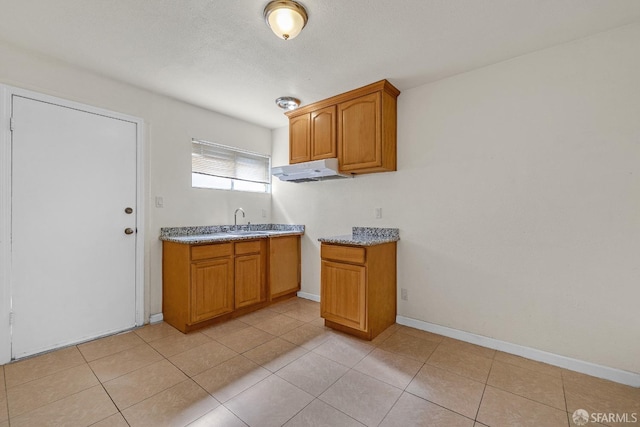 kitchen featuring a sink, brown cabinets, light tile patterned floors, baseboards, and under cabinet range hood
