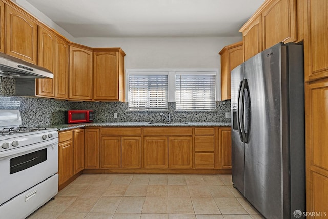 kitchen featuring a sink, under cabinet range hood, tasteful backsplash, white gas range, and stainless steel fridge with ice dispenser