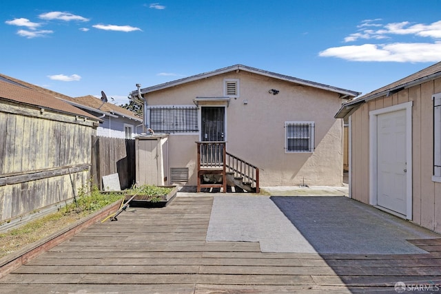 rear view of house featuring stucco siding, fence, and a deck