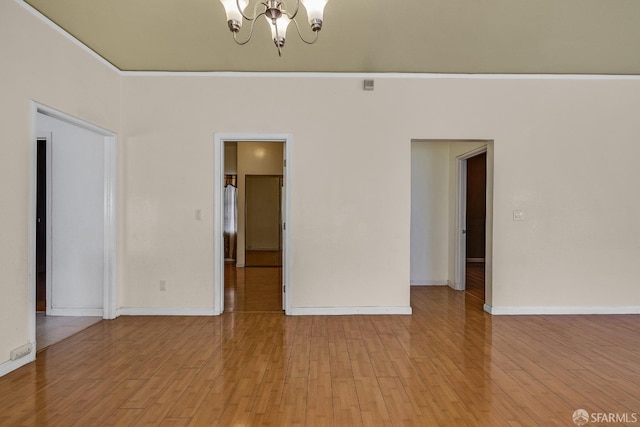 spare room with light wood finished floors, baseboards, and a notable chandelier