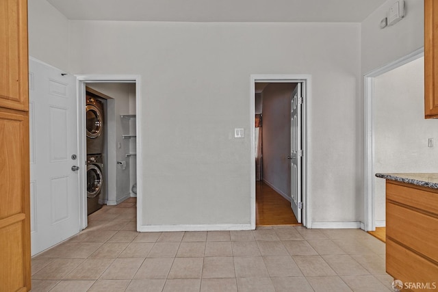 unfurnished bedroom featuring light tile patterned flooring, stacked washer / drying machine, baseboards, and a walk in closet