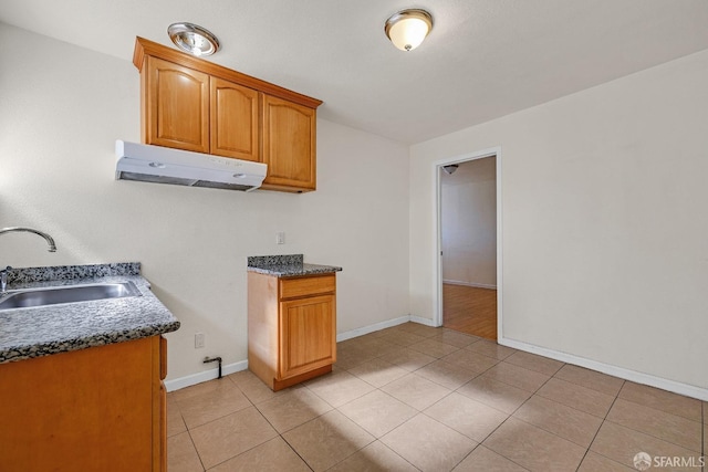 kitchen with baseboards, under cabinet range hood, a sink, and light tile patterned floors