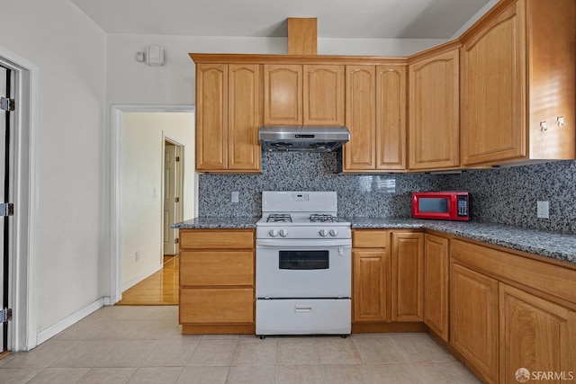 kitchen featuring dark stone countertops, tasteful backsplash, white appliances, under cabinet range hood, and light tile patterned flooring