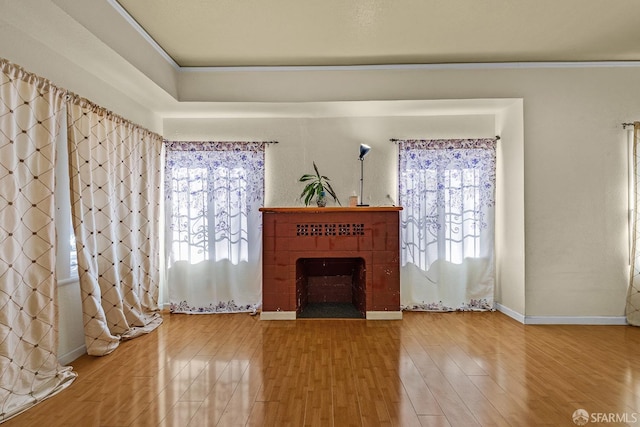 unfurnished living room featuring baseboards, wood finished floors, ornamental molding, and a brick fireplace