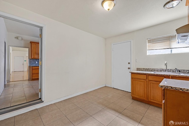 kitchen with brown cabinetry, a sink, light tile patterned floors, and tasteful backsplash