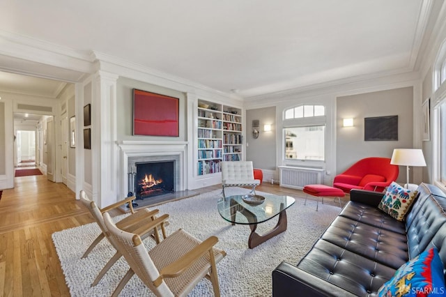 living room featuring ornamental molding, radiator heating unit, built in features, and light wood-type flooring