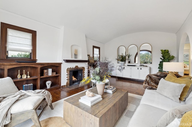 living room featuring a healthy amount of sunlight, vaulted ceiling, a brick fireplace, and light parquet floors