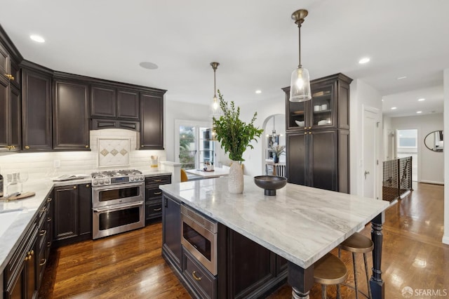 kitchen featuring a kitchen island, appliances with stainless steel finishes, dark wood-type flooring, and decorative light fixtures