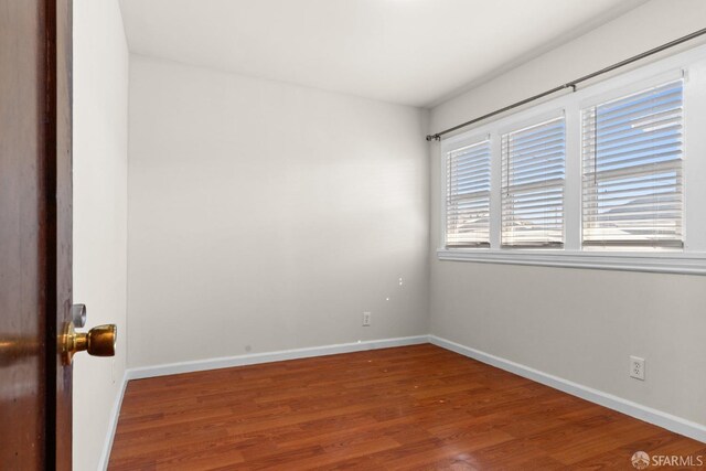 spare room with baseboards and wood finished floors