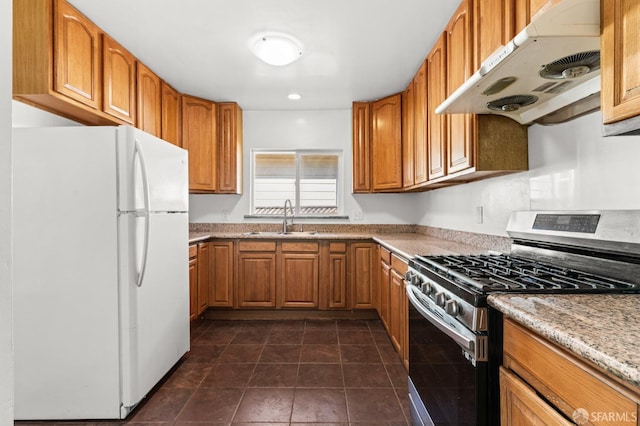 kitchen featuring under cabinet range hood, a sink, freestanding refrigerator, brown cabinetry, and gas stove