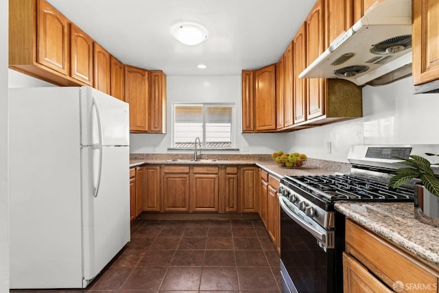 kitchen featuring gas range, brown cabinets, freestanding refrigerator, under cabinet range hood, and a sink