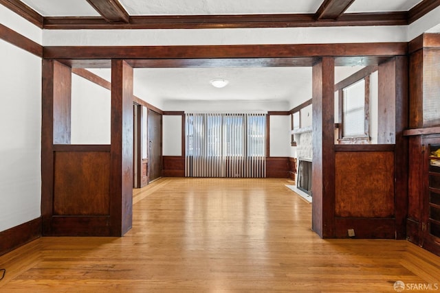 empty room featuring wood walls, a fireplace, wood finished floors, and wainscoting