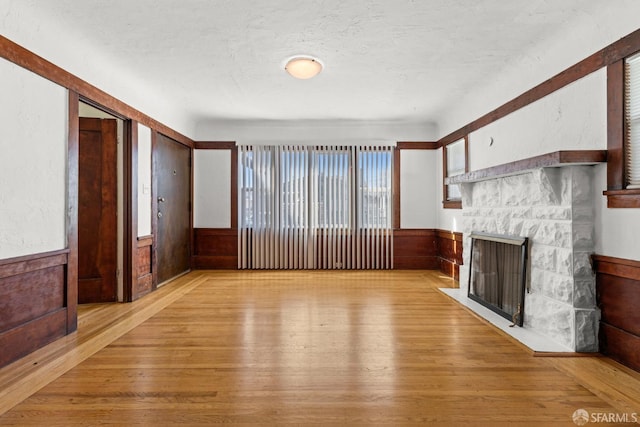 unfurnished living room featuring a wainscoted wall, a textured ceiling, a fireplace, and light wood-style flooring