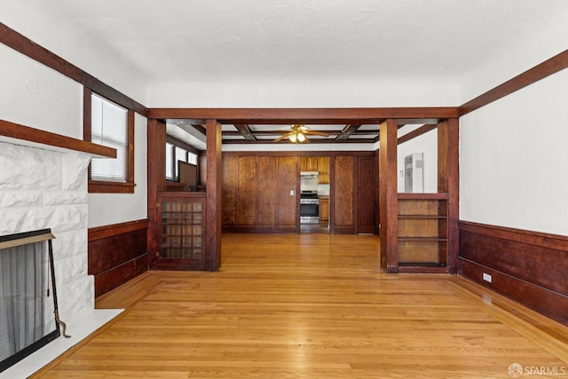 unfurnished living room with wood walls, wainscoting, a fireplace with flush hearth, and light wood-style flooring